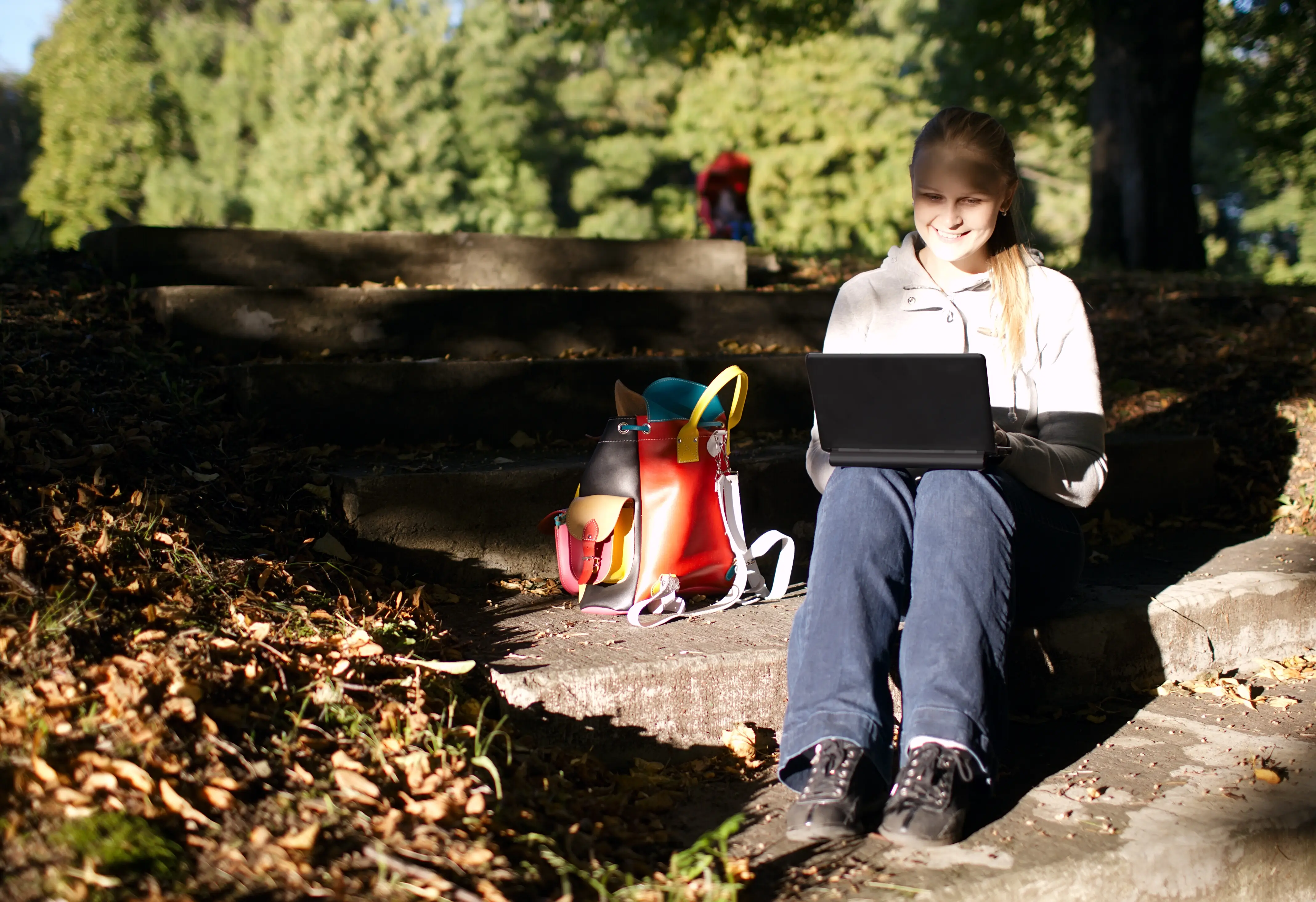 A happy woman sits on steps in a park using a laptop.